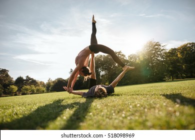 Outdoors shot of healthy young man lying on grass and balancing woman. Fit couple doing acrobatic yoga exercise in park. - Powered by Shutterstock