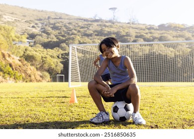 Outdoors, Smiling boy sitting on soccer ball on school field with goal in background. Sports, football, childhood, happiness, outdoor, exercise - Powered by Shutterstock