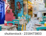 Outdoors traditional tavern restaurant in Greece, Tinos island Hora town Cyclades. Multicolor building, empty chair table, paved alley. Travel