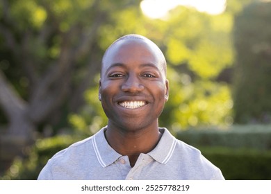 Outdoors, young African American man smiling in sunlit garden. Lush greenery background creating a serene atmosphere, with vibrant plants and flowers adding to peaceful scene, unaltered - Powered by Shutterstock