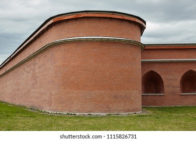 The outer side of the brick wall of an ancient fortress of red brick with arches against the cloudy sky.