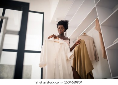 Outfit for day. Curly fashionable woman choosing outfit for day early in the morning