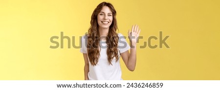 Outgoing comfortable relaxed friendly casual european woman curly haircut waving raised palm say hello introduce herself become new member smiling broadly greeting hi gesture yellow background