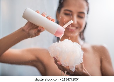 Outgoing girl putting shower gel on puff. She taking hot shower
