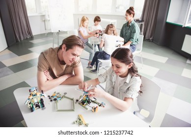 Outgoing little girl and satisfied male teacher making helicopter. Woman and children sitting opposite them. Modern education concept 库存照片