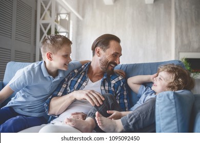 Outgoing Man Telling With Cheerful Kids While Sitting On Cozy Sofa. Glad Family Concept