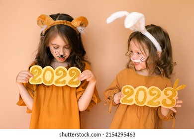 Outgoing year of Tiger and New Year of the Rabbit. Sad child with tiger makeup holds number 2022, and baby in guise of rabbit holds 2023. Painted face of people with aquagrim in image of animal. - Shutterstock ID 2154295463