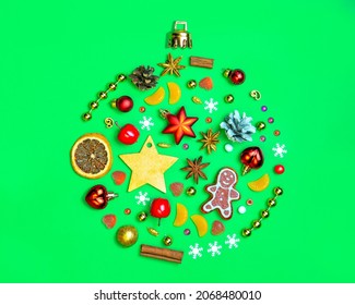 The outline of a Christmas ball on a bright green background. Filled with gingerbread, spruce twigs, toys for the Christmas tree, cinnamon. The concept of Christmas gifts. Greeting card for Christmas.