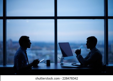 Outlines of two businessmen working late in office