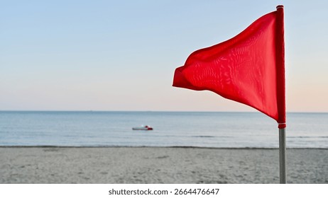 Out-of-focus red triangular warning flag in the foreground, with a sharp focus on the calm but potentially dangerous sea in the background. A pedal boat floats near the horizon.	
