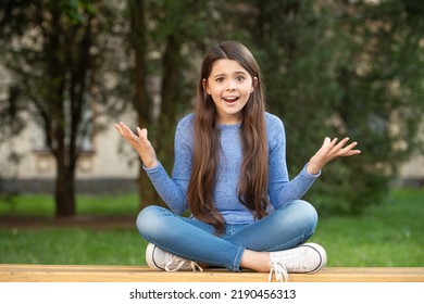Outraged Girl Teenager Shrugging Shoulders Sitting Legs Crossed On Bench Outdoors, Outrage