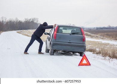 Outraged guy wanting to turn his car on back from anger, his broken car cannot be repaired because his insurance doesn't want to cover the damage, red warning triangle on frozen snowy winter road