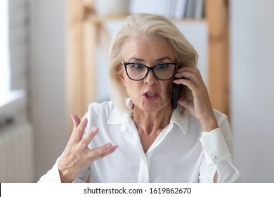 Outraged mature businesswoman talking by phone arguing with client feels irritated, 60s employee disputing having unpleasant conversation with customer, business problem solution, bad service concept