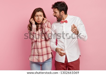 Outraged young man shouts at guilty woman and reproaches about wrong doing, blames, dissatisfied woman plugs ears, ignores loud yelling of angry husband or boss, isolated over pink background. Stock photo © 