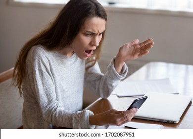 Outraged young mixed race girl looking at mobile phone screen, annoyed by bad application work or received scam spam message. Stressed displeased shocked millennial woman irritated by device crash.