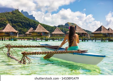 Outrigger Canoe - woman paddling in traditional French Polynesian Outrigger Canoe for recreational activity and watersport competition. Bora Bora with  overwater bungalow resort hotel sport lifestyle 