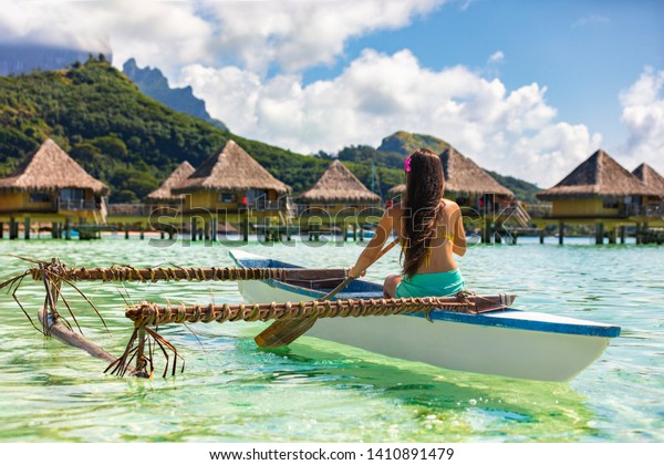Outrigger Canoe - woman paddling in traditional French\
Polynesian Outrigger Canoe for recreational activity and watersport\
competition. Bora Bora with  overwater bungalow resort hotel sport\
lifestyle 