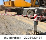 Outriggers of heavy all-terrain mobile crane at construction site. Crane work execution area fenced with a signal tape. Exclusion dropped zone
