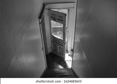 An outside front deck is seen through, a broken window in a door, of an old abandoned house. In black and white.