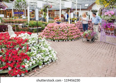 Outside Of Garden Center With Many Types Of Plants And Flowers And Couple Pushing A Trolley