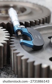 Outside micrometer precision measuring tool placed on top of industrial steel gears for quality control.