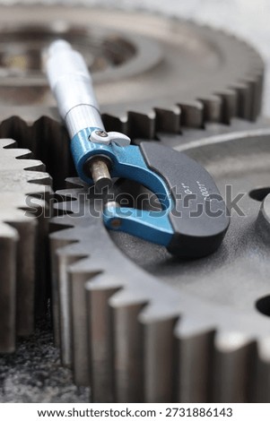 Outside micrometer precision measuring tool placed on top of industrial steel gears for quality control.