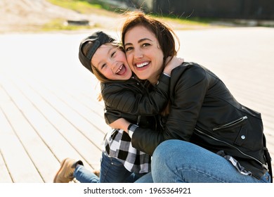 Outside portrait of mom with daughter wearing leather jackets hugging and smiling in sunlight . High quality photo
