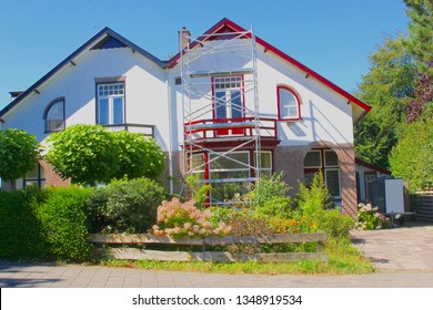 Outside Renovation And Painting Exterior Walls, Doors And Window Frames Of Old Dutch House With Scaffold Tower In Front Yard Garden, Netherlands