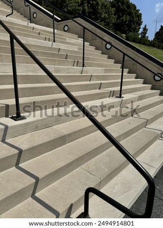 Outside sunny bright day with concrete stairs from a low angle perspective with handrails, green trees, shadows and blue sky with clouds