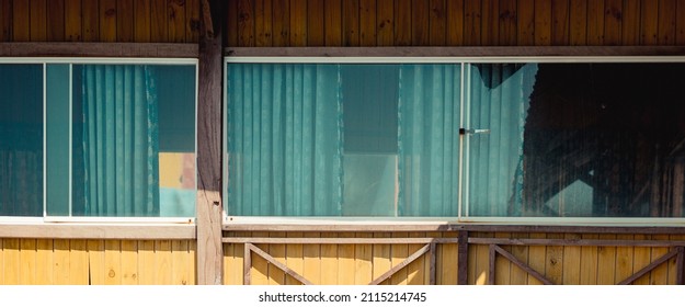Outside view facade. Wooden yellow brown boards material, country house, panoramic window glass nature reflect, curtains inside. Summer day warm light mood. Cozy home interiors, leisure, eco building