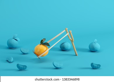 Outstanding mandarin orange in a slingshot surrounded by oranges painted in blue on blue background. Minimal fruit idea concept.
