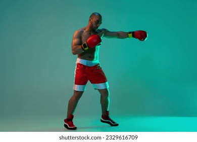 Outstretched fist. Young male boxer in red gloves training, practicing on blue green background in neon light with copyspace for ad. Health, sport, motion concept. Full length image - Powered by Shutterstock