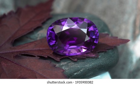 An oval amethyst placed on a maple leaf and black pebbles.