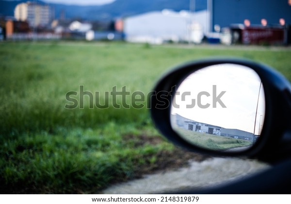 Oval mirror car view on a blurry green\
industrial landscape in the\
background