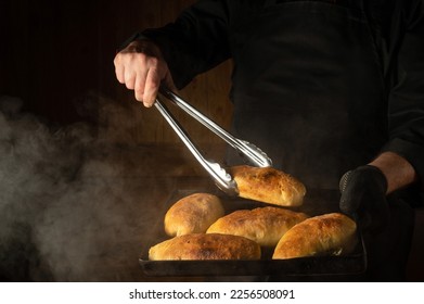 Oven baked buns on a hot baking sheet in the chef hand in glove. The chef takes a hot bun with a culinary tongs. - Powered by Shutterstock