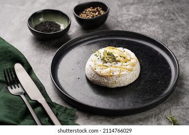 Oven Baked Camembert Cheese With Black Pepper, Sesame Seeds On Black Plate, Grey Concrete Surface. Homemade Grilled Brie With Thyme, Dark Table Setting