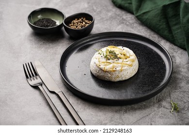 Oven Baked Camembert Cheese With Black Pepper, Sesame Seeds On Black Plate, Grey Concrete Surface. Homemade Grilled Brie With Thyme, Dark Table Setting