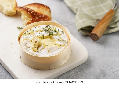 Oven baked camembert cheese with lye baguette bread on marble board, grey concrete surface. Homemade grilled brie with thyme on green checkered kitchen towel