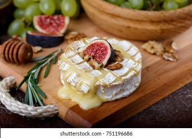 oven baked Camembert on wooden board, branch of green grapes in bowl of natural wood, slice of figs, rosemary