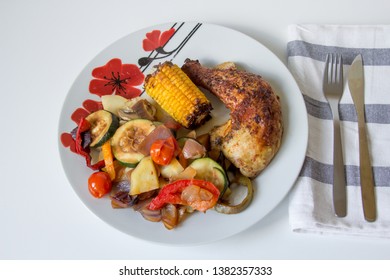 Oven Baked Chicken Plated With Roasted Vegetable, Fork And Knife On Tea Towel On Side