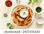 Oven baked potato wedges with sauce over light stone background. Top view, flat lay