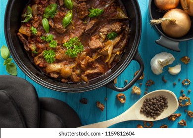 Oven Cooked Meat Casserole In Cast Iron Dutch Oven With Herbs On Turquoise Wooden Background , Top View