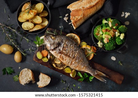 Oven fresh gilthead baked with herbs and lemon, served with potatoes and buttered broccoli with almond flakes