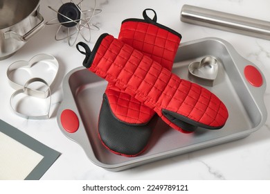 Oven mitts lying in a baking pan surrounded by kitchen utensils