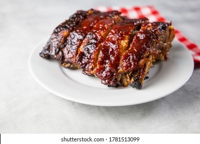 Oven-baked barbecue ribs with sauce on a white plate with a red checkered picnic napkin for a family barbecue