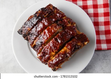 Oven-baked barbecue ribs with sauce on a white plate with a red checkered picnic napkin for a family barbecue