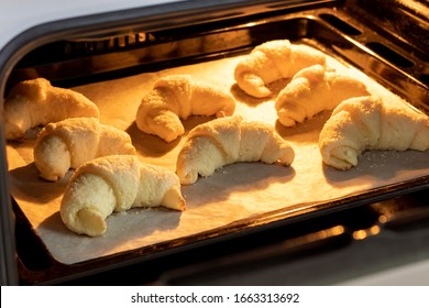 Oven-baked sugar-frosted croissants on a baking sheet covered with parchment paper. Sweet bagels from a cottage cheese dough baked in a hot oven. The process of making curd bagels or croissants - Powered by Shutterstock