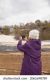 An  Over Eighty Years Old Women Spend A Fall Day In Their Home Town Bracebridge, Ontario. Se Is Taking Phone Picture Of The Waterfall In Muskoka .