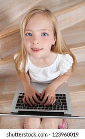 Over Head Close Up View Of A Young Girl Child Using A Laptop Computer While Sitting On Wooden Steps At Home, Looking Up At Camera And Smiling.