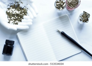 Over head flat lay view of a white and gold chic desktop. Open notebook, pen and ink, gold office supplies and  open hands holding glitter.